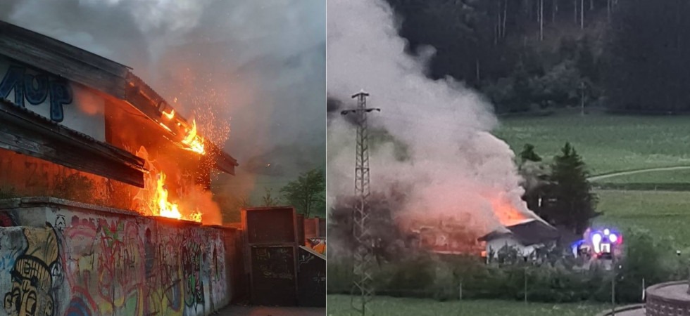 Una colonna di fumo e le fiamme avvolgono il tetto di un edificio, vigili del fuoco in azione