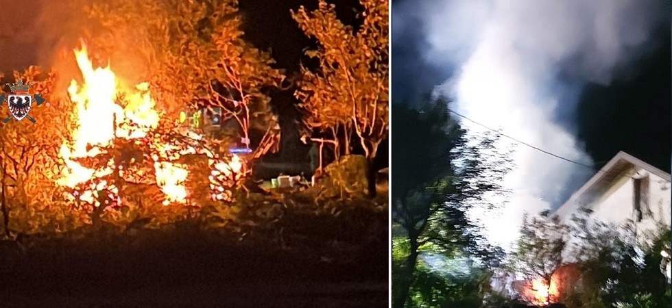 Fiamme alte e una grossa colonna di fumo, legnaia a fuoco nella notte a poca distanza da un edificio