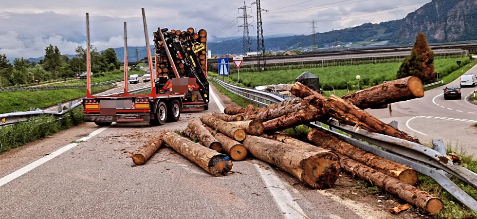 Il rimorchio colpisce un cartello e si sbilancia: grossi tronchi cadono sull'asfalto, strada bloccata