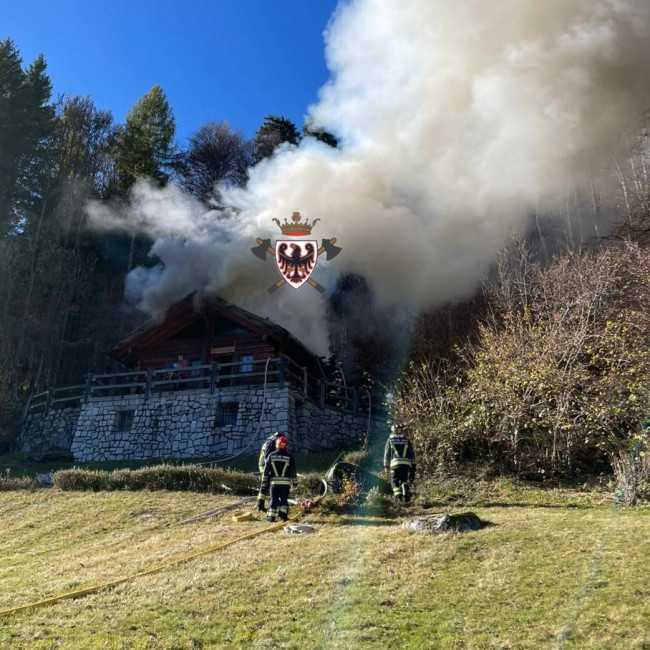 Fiamme dal tetto della baita e una colonna di fumo si alza in cielo ...